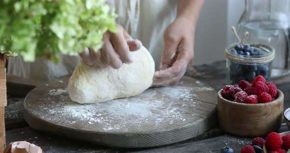 The woman kneads the dough with her hands. Female hands and raw dough on a wooden background. alt