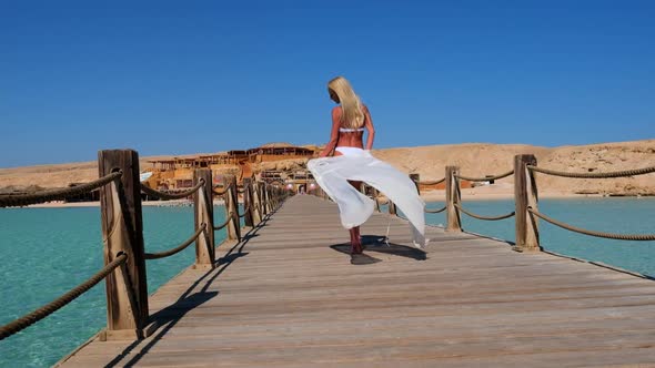 Pretty Young Woman in White Pareo Standing on Pier Near Sea alt
