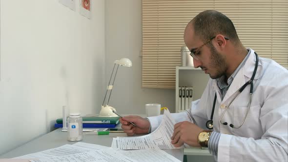 Busy Male Physician Working with Papers and Having Phone Conversation in His Office alt