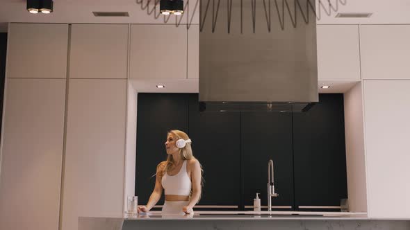 A Young Happy Blonde Woman Dancing with Headphones in the Beautiful Kitchen alt