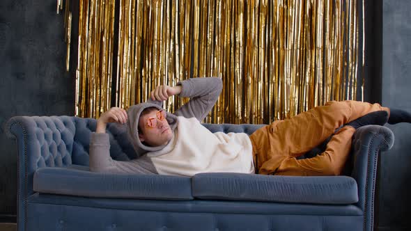 Stylish Man in Hoodie with Ears and Sunglasses Lying on Sofa alt
