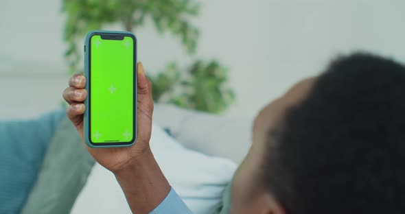 Man Lying on Couch with Modern Smartphone in His Hand While Looking on Mock Up Screen with Trecking