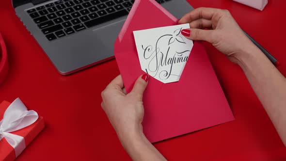 Female Hands Open Festive Envelope and Take Out a Greeting Postcard with March 8Th alt