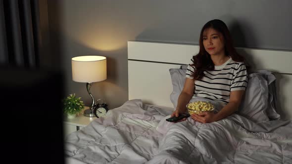 young woman watching TV on a bed at night