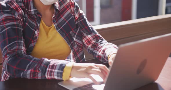 Mixed race woman working on laptop wearing coronavirus mask alt
