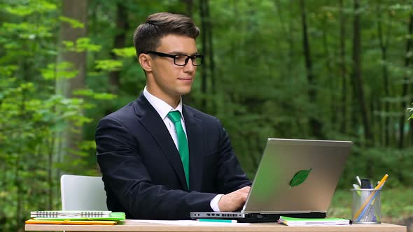 Young Smiling Office Worker Typing on Laptop Sitting in Green Park, Slow-Mo alt