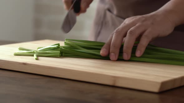 Hands of chef chopping green leek vegetable or spring onions on wood cutting board