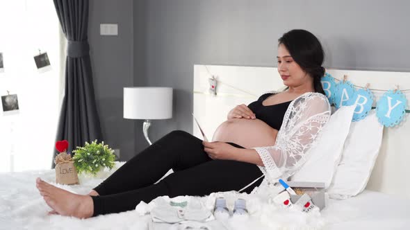 woman looking ultrasound photo and pat her pregnant belly on the bed