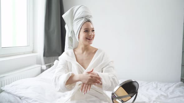 Positive Young Woman in White Bathrobe Apply Cream on Hands