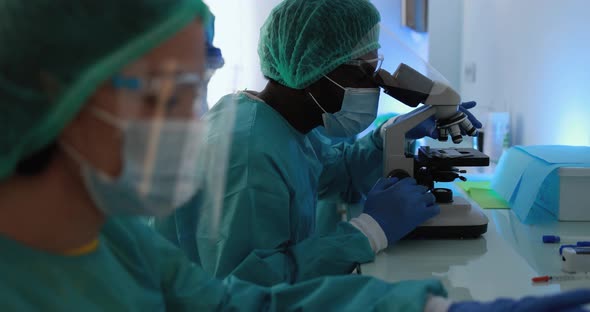 Medical workers in hazmat suit working with laptop computer and micoroscope alt