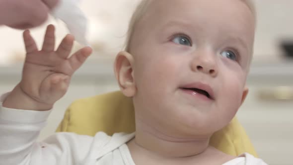 Father Wiping Face of His Oneyearold Son with Baby Wipes After Feeding Him in the Kitchen alt