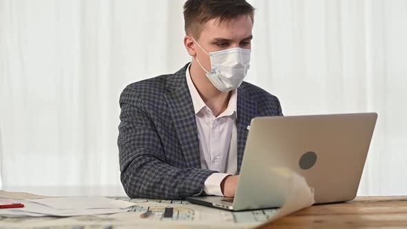man has put protective mask on face and is working with drawings and plans alt