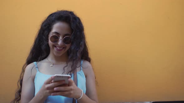 Smiling Teenage Girl with Sunglasses and Smartphone Texting in City