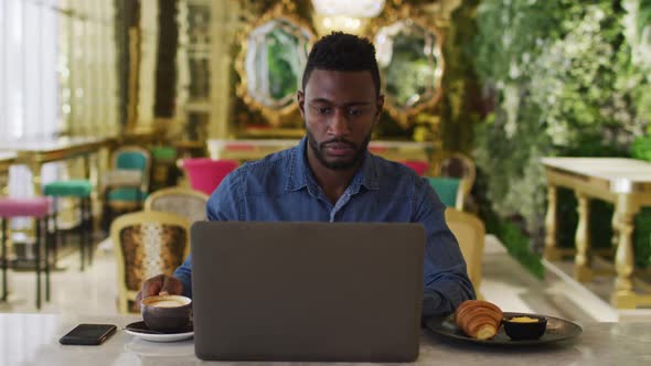 African american businessman using laptop drinking coffee in cafe alt