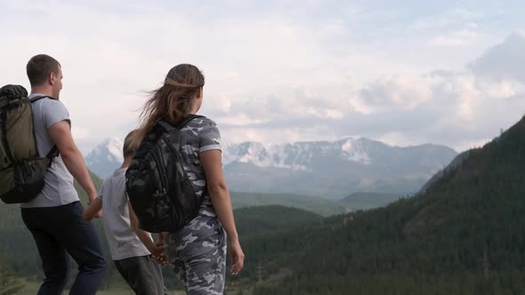 Happy Family with Son Raise Their Hands Up and Rejoice Standing on the Peak of the Mountain alt