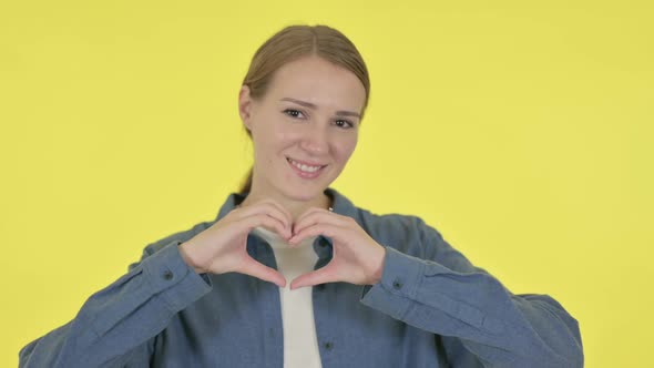 Young Woman Showing Heart Shape By Hands on Yellow Background alt