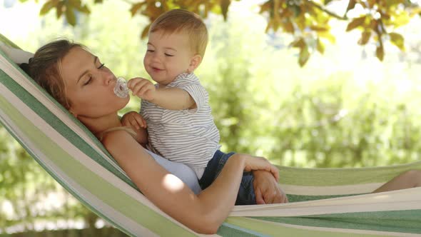 smiling happy mother hugs and cuddle her little baby son, relaxing  lying together in the hammock. C
