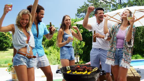 Group of friends dancing and having drinks while preparing barbeque alt