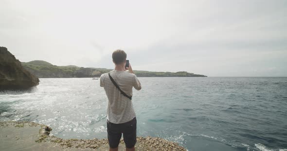 Dolly Medium Shot of a Male Tourist Taking Pictures with His Phone of the View at Broken Beach Pasih alt
