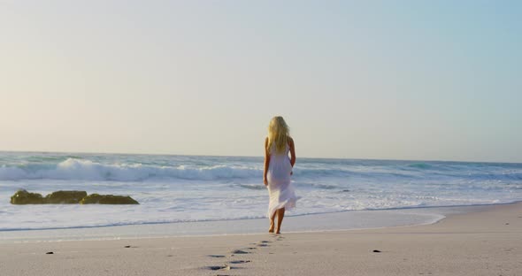 Woman walking towards sea on beach during sunset 
