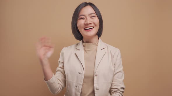 Happy asian business woman waving her hand for greeting and looking at camera isolated