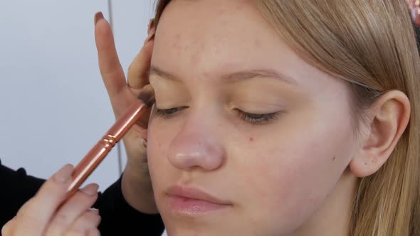 A Professional Makeup Artist Applies a Base Under Eye Makeup to the Face of a Young Beautiful Girl alt