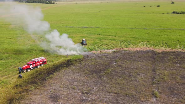 A Fire Truck and a Tractor on the Edge of a Burnt Field with Smoke alt
