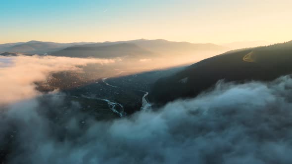 View from above of vibrant landscape of foggy clouds covering mountain hills and village alt