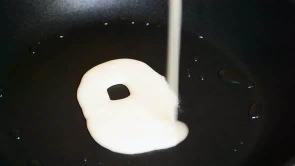 Liquid pancake mix gets poured into a black greasy frying pan. Person swinging the pan around in ord alt