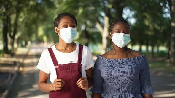 Two Sad African American Young Women in Covid Face Masks Standing in Summer Park Sighing Looking alt
