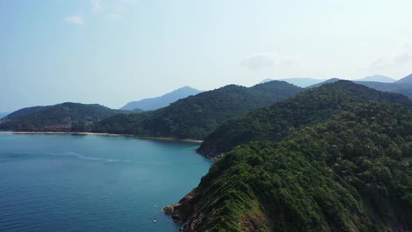 Mountains of tropical islands with lush vegetation and rocky shoreline washed by calm sea surface re alt
