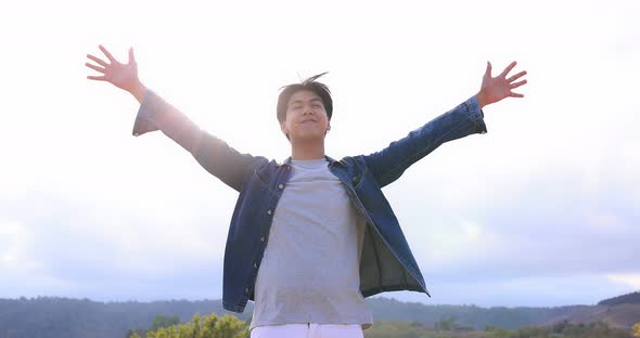 Freedom Asian young man raising hands on the top at the mountain. alt