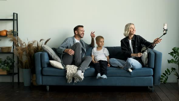 Happy family adult parents with cute children relax on sofa using funny smartphone apps