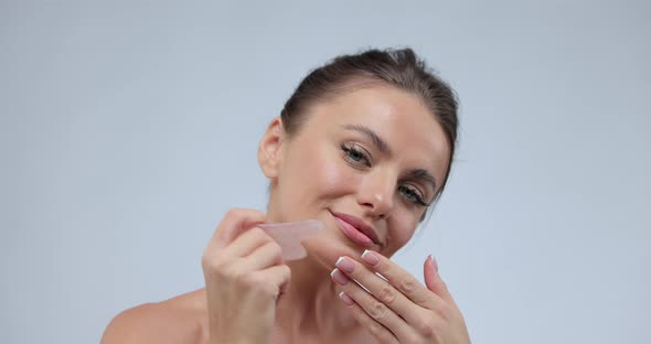 Caucasian Young Model Without Makeup Doing a Facial Massage Using a Gua Sha Stone While Looking at alt