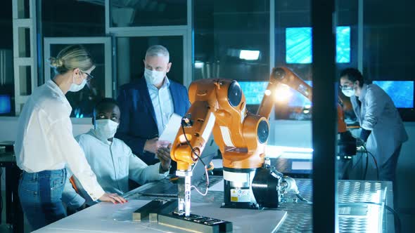 Science Workers in Face Masks Working with Robotic Arms alt