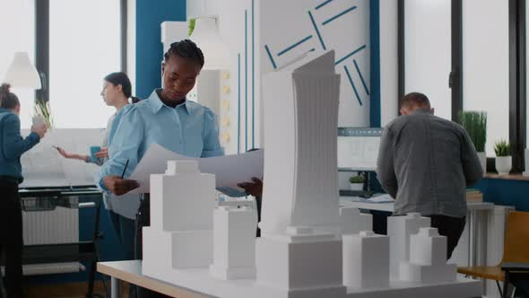 Portrait of African American Architect Looking at Blueprints Plans to Work on Building Model alt