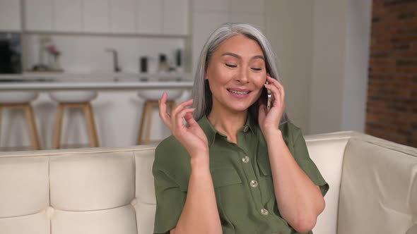 Cheerful Middleaged Greyhaired Asian Women Chatting with Friend on Mobile Phone