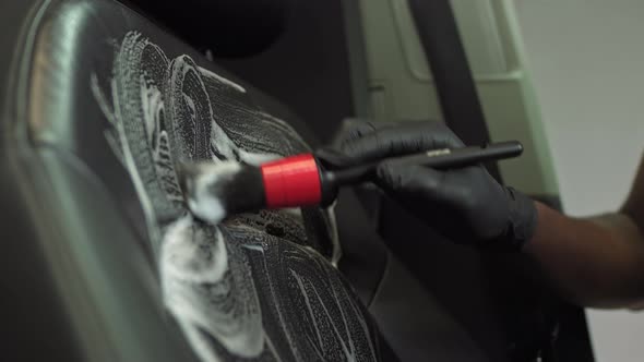 Hand of a Black African American with a Brush Cleans the Leather Seat of a Car alt