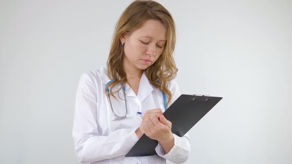 A doctor in a medical gown fills out paperwork on a tablet alt