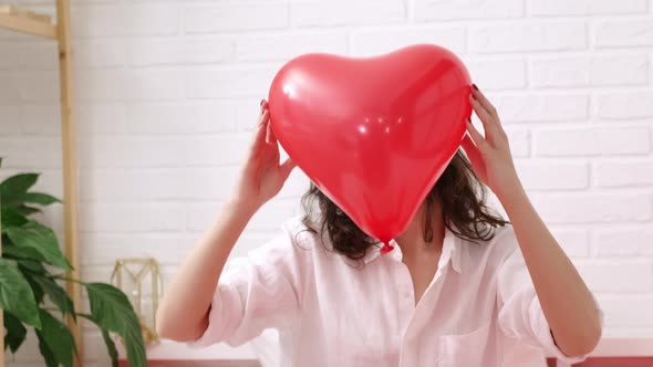 Red Heart Shaped Balloon Close Up in Hands of Brunette Smiling Girl on Valentines Day alt