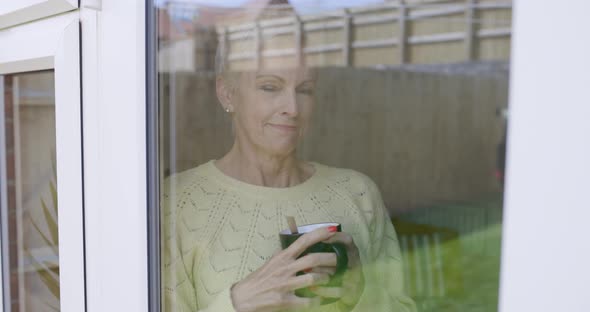 Mature woman stirring in coffee cup leaning on window