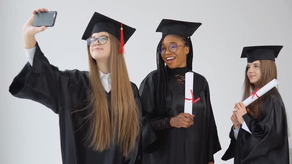 Three Young Happy Graduate Women of Different Nationalities Stand Together and Take a Selfie with alt