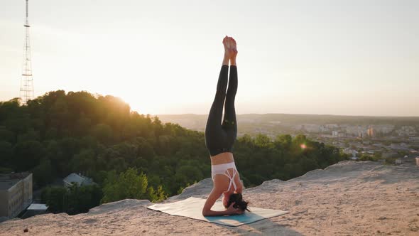 Woman Yoga Stays in Shirshasana Position on Top of Hill at Sunset