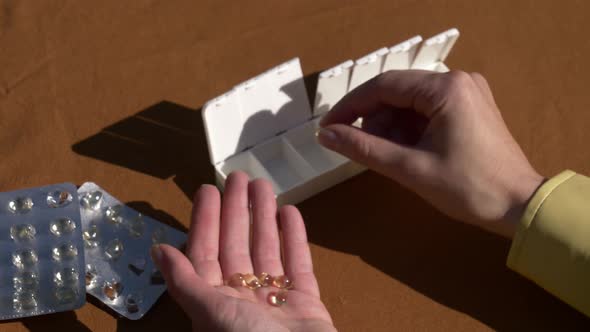 Female hand sorting pills in pillbox on brown background