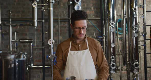 Portrait of happy caucasian man working at gin distillery using equipment and smiling to camera alt