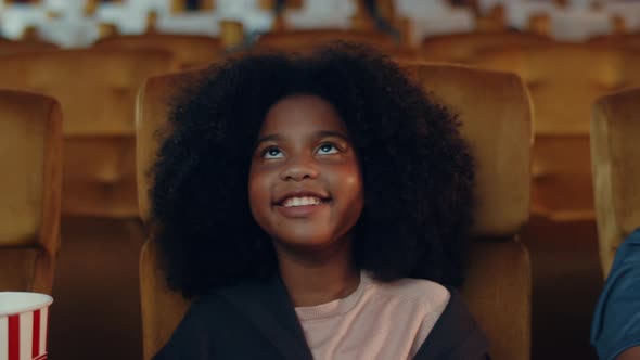 Attractive cheerful young black african girl laughing while watching film in movie theater.