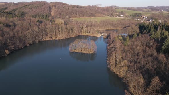 Aerial footage of a blue lake within a brown winter landscape at sunset. alt