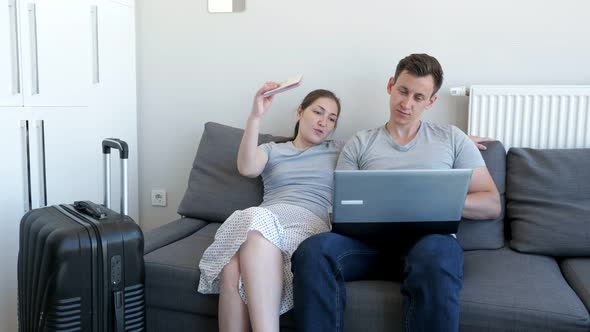 Man and Woman Choosing and Booking Tour and Hotel Sitting on Sofa with Passports and Suitcase. alt