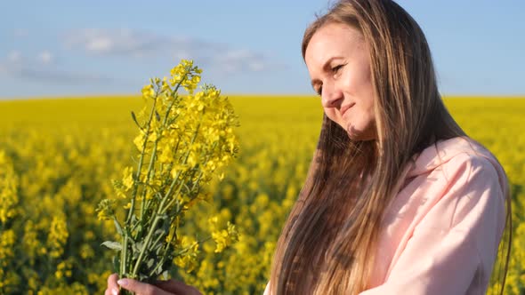 Attractive Blonde of European Appearance Admires a Bouquet of Rapeseed Flowers alt