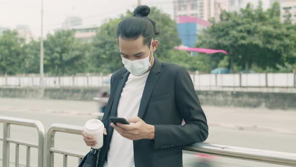 Asian businessman wearing a face mask holding coffee cup and using phone.